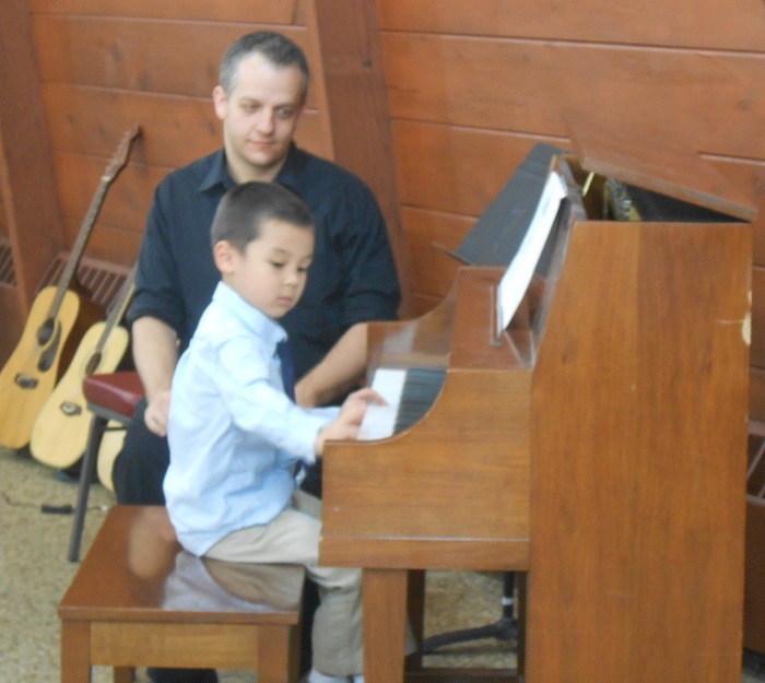 Mr Dan watches as pupil plays the piano during the AMA recital